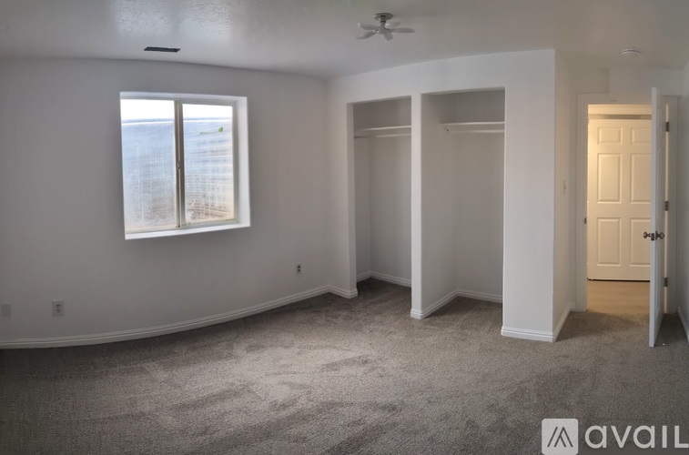A room with a carpeted floor, a ceiling fan, and a window with a view of a building outside.