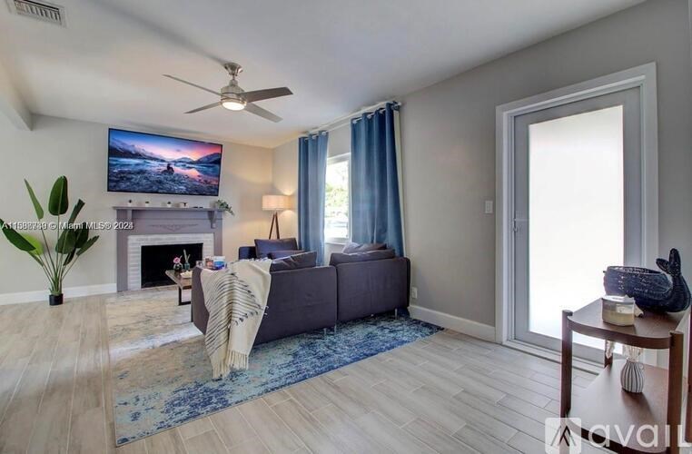 A living room with a grey couch, a fireplace, a TV, a fan, and a plant.