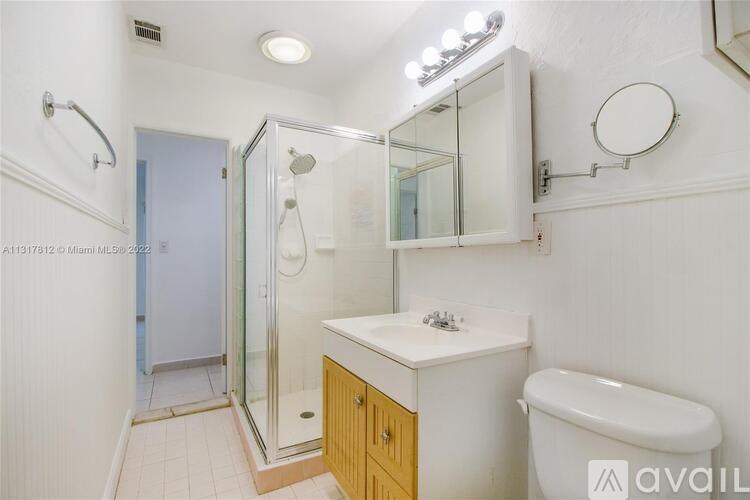 A bathroom with a white sink, a toilet, a mirror, a shower, and a wooden cabinet.