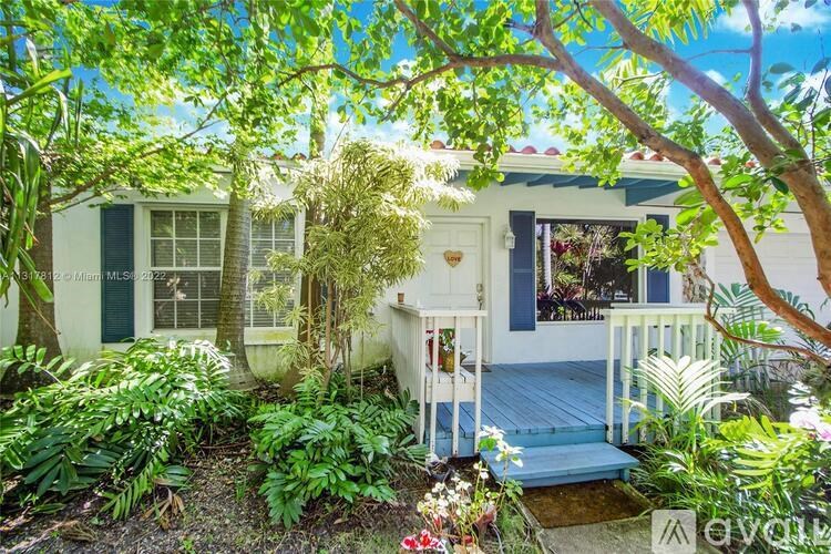 A house with a white porch and a green door is surrounded by lush greenery.