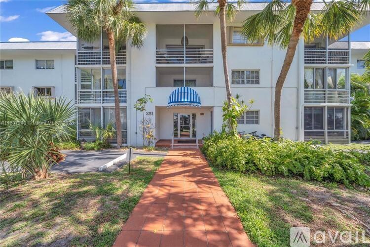 A white building with a blue awning and a brick pathway leading to the entrance.