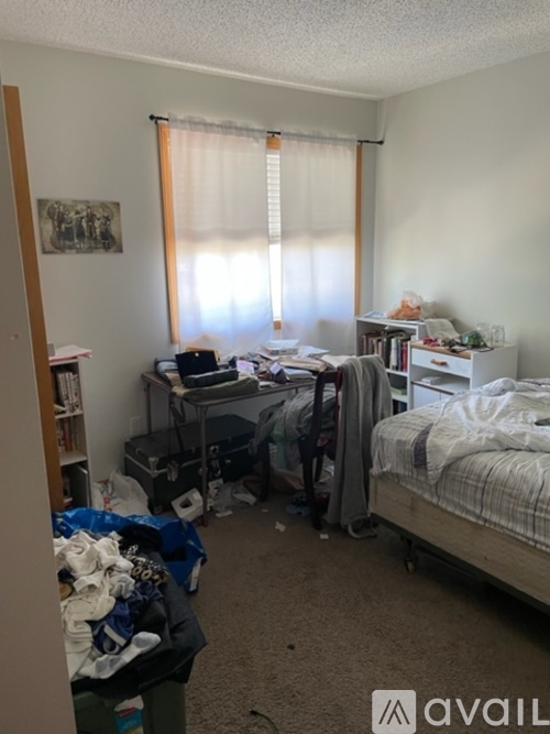 A messy bedroom with a bed, desk, and clutter.