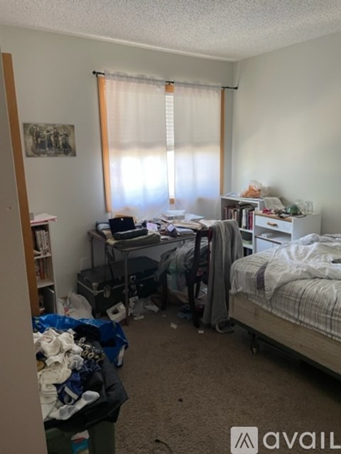 A messy bedroom with a bed, desk, and clutter.