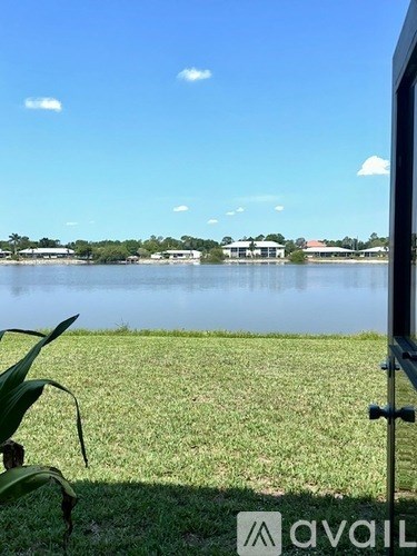 A grassy field with a lake and buildings in the distance.