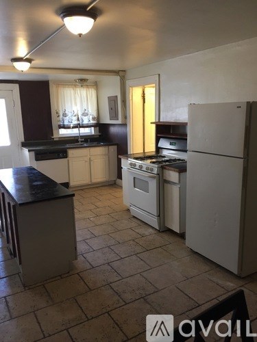 A kitchen with a white fridge, black countertops, and a window with curtains.