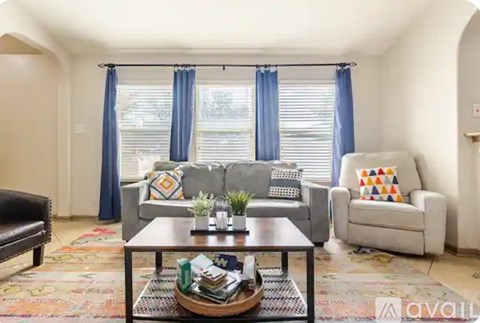 A living room with a grey couch, a black bench, a coffee table with a plant on it, and a window with blue curtains.