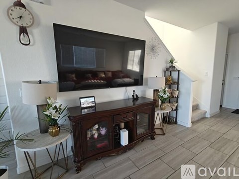 A living room with a wooden cabinet, a clock, a plant, and a painting on the wall.