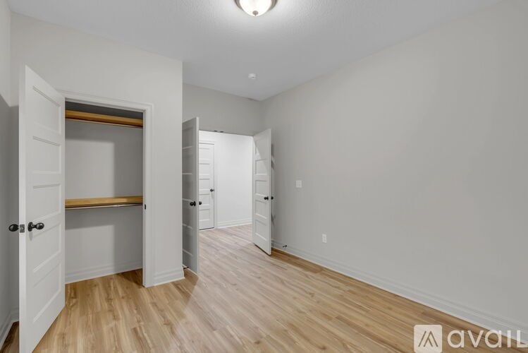 A room with a wooden floor and white walls, with a door on the left and a window on the right.