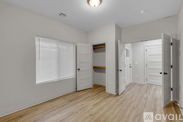 A room with white walls and wooden flooring, with a window covered by white blinds.