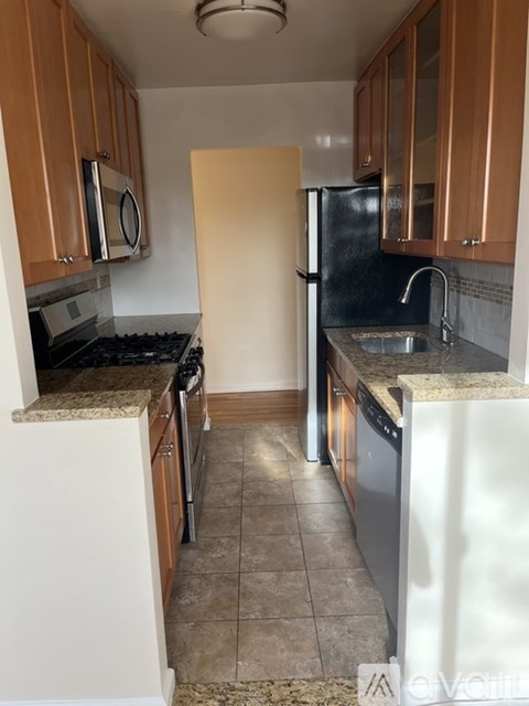 A kitchen with a black refrigerator, white countertops, and brown cabinets.