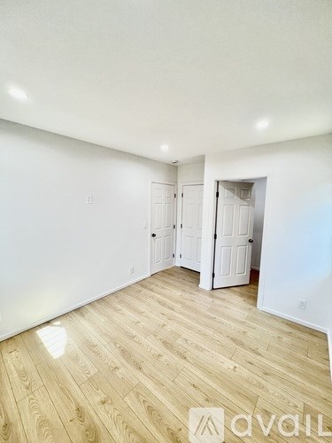 A room with wooden flooring and white walls, with a doorway leading to another room.