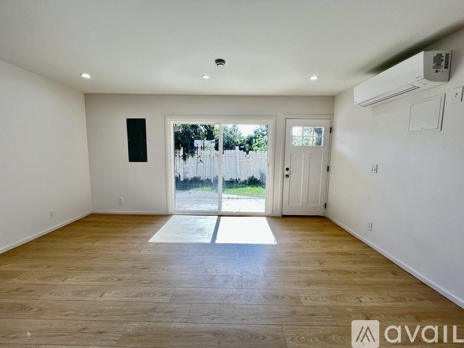 A spacious room with wooden floors and a sliding glass door leading outside.