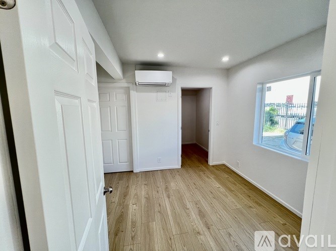 A room with a window, wooden floor, and a white door.
