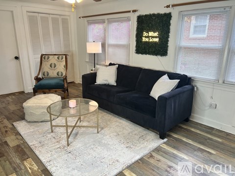 A living room with a black couch, a glass table, and a chair with a green cushion.