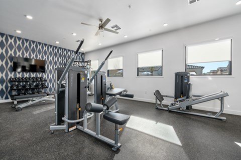A spacious gym with a variety of equipment including a squat rack, leg press machine, and a bench press at Allero 59 Apartments, Phoenix, AZ, 85035