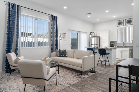 A modern living room with comfortable seating and a glass coffee table with a view into the spacious kitchen with stainless steel appliances and a kitchen island at Allero 59 Apartments, Phoenix 85035