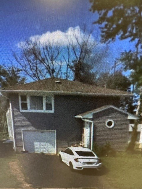A white car is parked in front of a grey house.