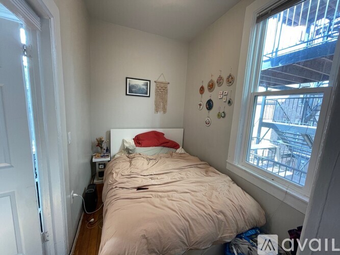 A small bedroom with a bed, a window, and a wall hanging.