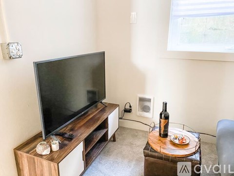 A living room with a television and a glass table with food and a bottle of wine on it.