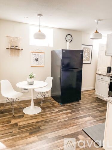 A kitchen with a black fridge, white chairs and a white table.