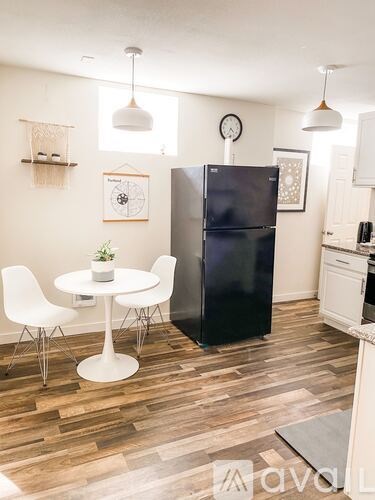 A kitchen with a black fridge, white chairs and a white table.
