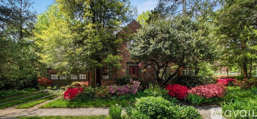 A house surrounded by green trees and red flowers.