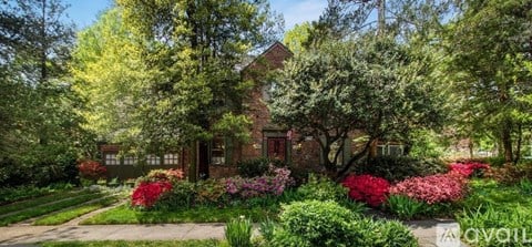 A house surrounded by green trees and red flowers.