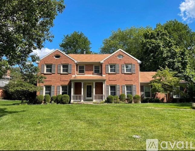 A red brick house with a porch and a tree in front.