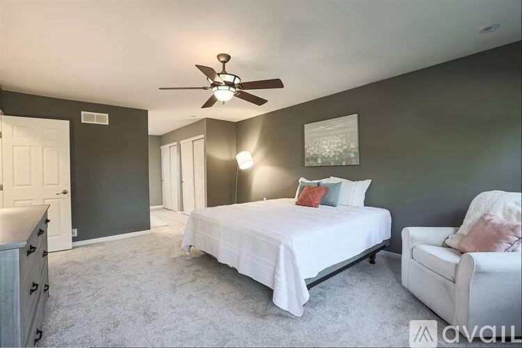 A bedroom with a bed, chair, and ceiling fan.