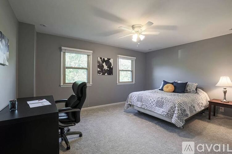 A bedroom with a bed, desk, chair, and ceiling fan.