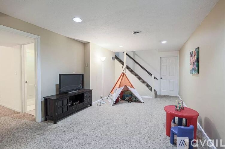 A room with a carpeted floor, a television, a red stool, and a tent.