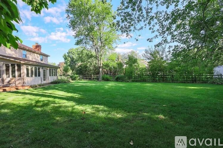 A large, well-kept lawn in front of a house with a tree and a fence.