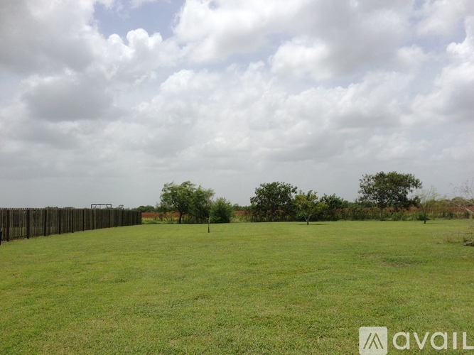 A grassy field with a fence and trees in the distance.