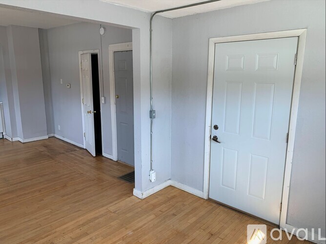 A room with a white door and a white wall with a pipe running along it.