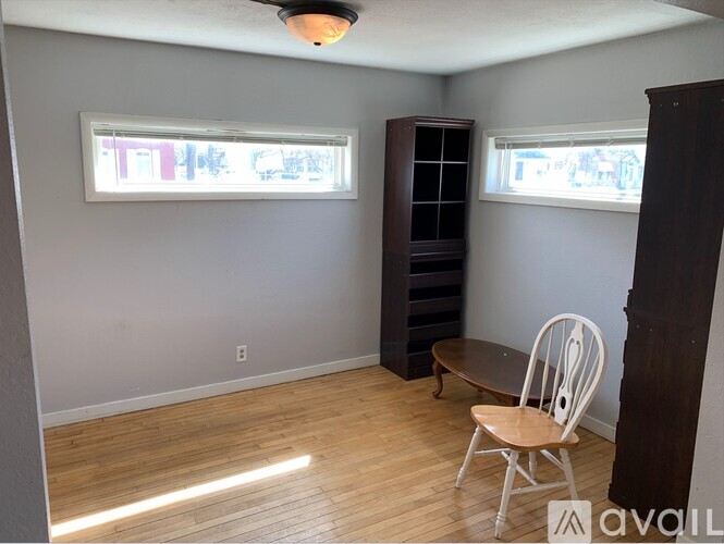 A room with a wooden floor, a white chair, and a cabinet.