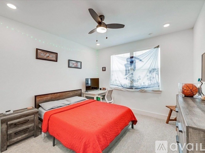 A bedroom with a red bedspread and a ceiling fan.