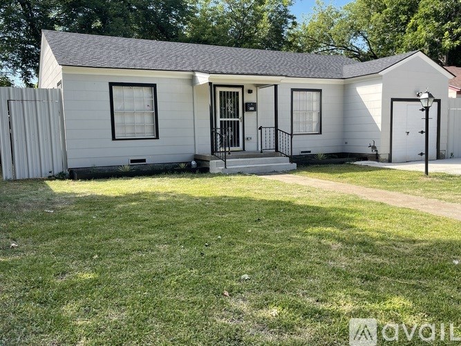 A white house with a black door and windows is surrounded by a green lawn.