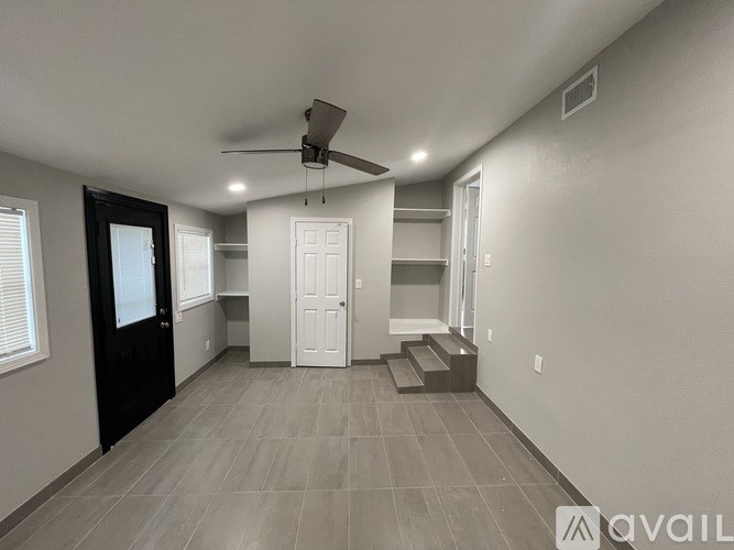 A spacious room with a ceiling fan and lighting, featuring a black door, a white door, and a built-in bench.