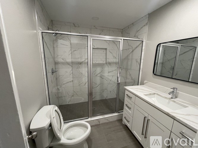 A white toilet is in a bathroom with a marble shower.