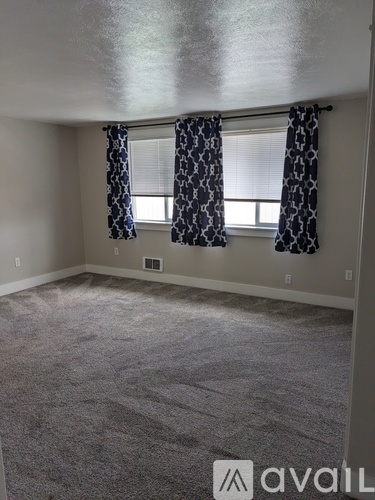 A room with a carpeted floor and a window with curtains.