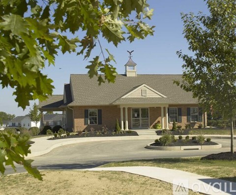A house with a brown roof and a white chimney is surrounded by trees and bushes.