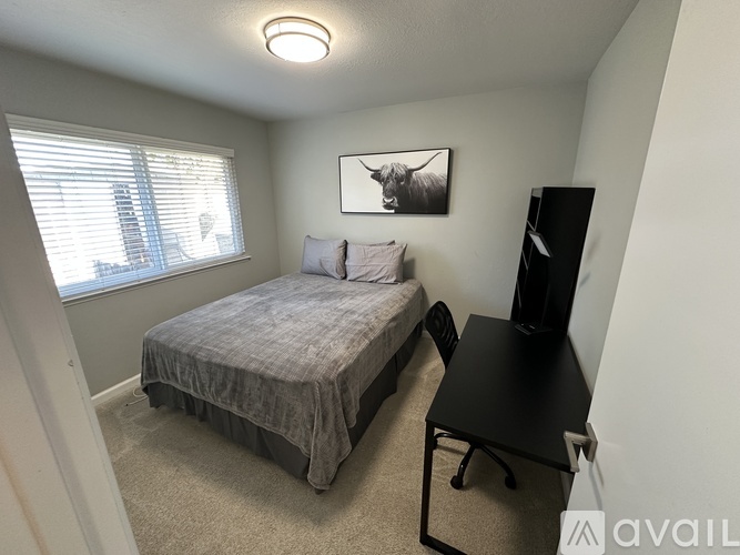 A bedroom with a bed, desk, and a window with blinds.
