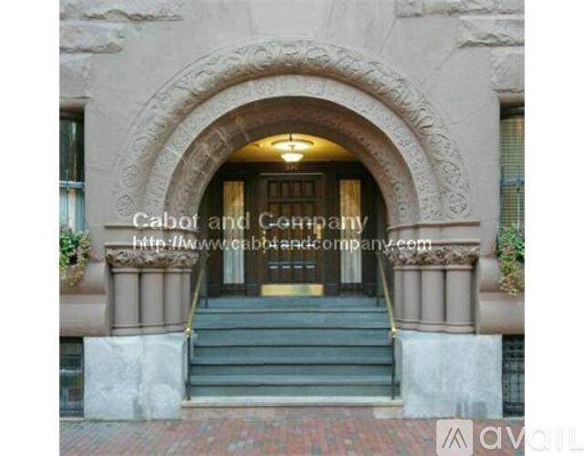 The image shows the entrance to a building with a stone archway and steps leading up to a set of double doors.