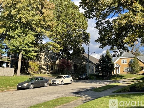 Two cars parked on a street with trees and houses in the background.