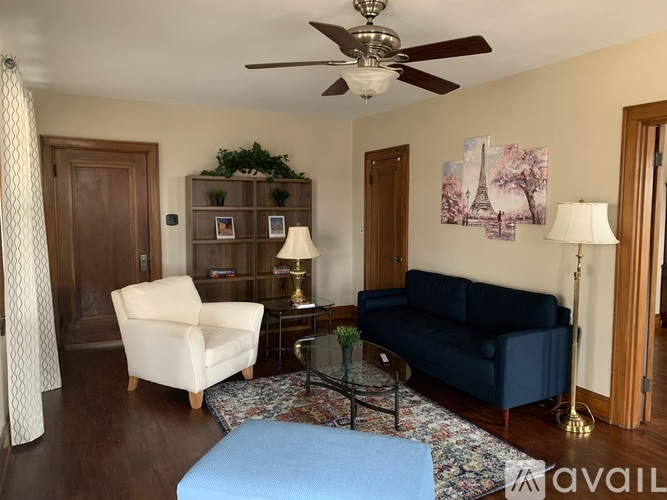 A living room with a blue couch, a white chair, a glass coffee table, and a ceiling fan.
