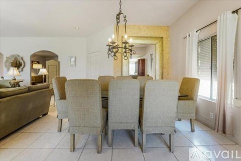 A dining room with a chandelier, a table with chairs, and a kitchen area in the background.