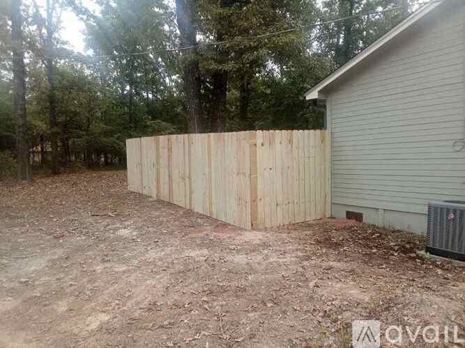 A wooden fence in a backyard with a house and trees in the background.