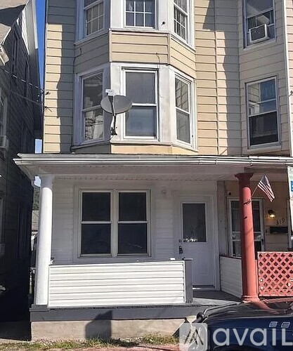 A two-story house with a white front porch and a satellite dish on the roof.
