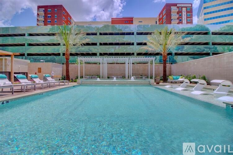 A large swimming pool with lounge chairs and palm trees in front of a multi-story parking garage.