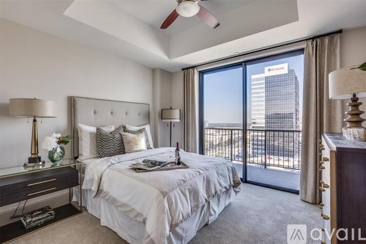 A bedroom with a large bed, a ceiling fan, and a view of a city skyline through the window.